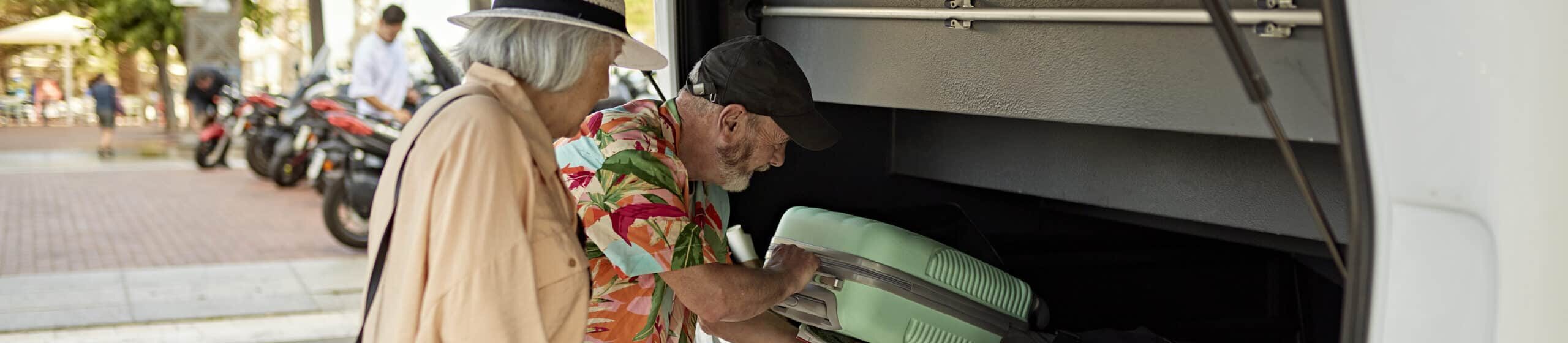 Senior tourists loading luggage into back of coach bus